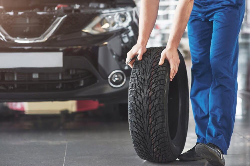 Dicas para prolongar a vida útil dos pneus do seu veículo 2 technician with blue workwear holding wrench tire while showing thumb up 2